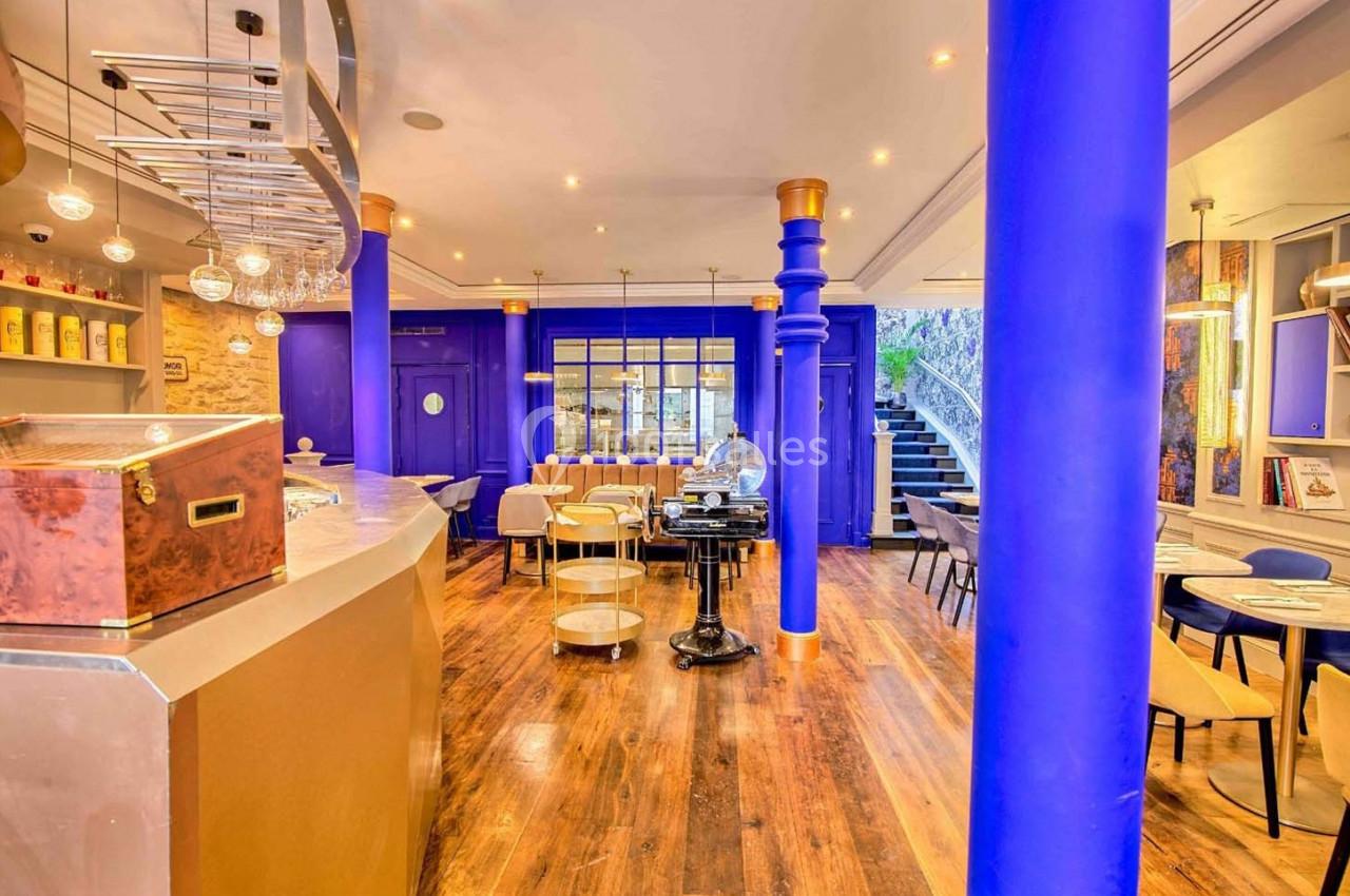 Intérieur d'un café moderne avec colonnes bleues, mobilier clair, parquet en bois et éclairage chaleureux.