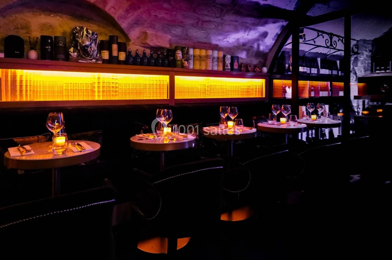 Salle de restaurant avec tables dressées, éclairage tamisé et étagères illuminées en arrière-plan.