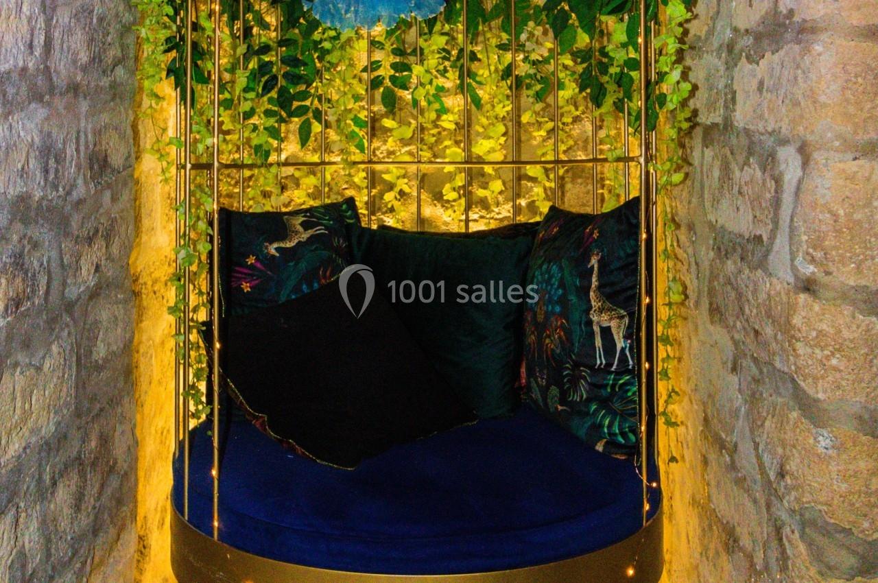 Balancelle dorée suspendue, entourée de fleurs, feuillages et éclairages chaleureux, dans une alcôve en pierre.