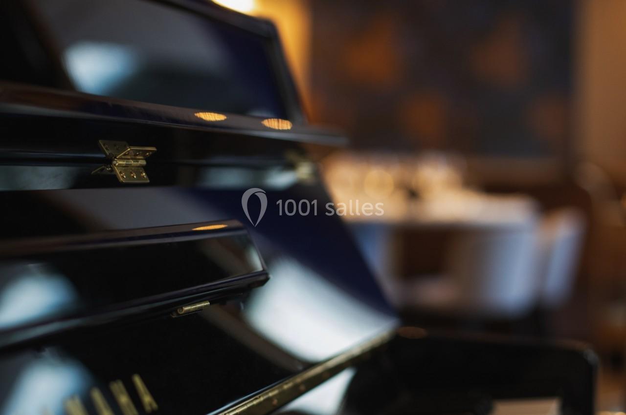 Clavier d'un piano noir brillant en gros plan, avec un arrière-plan flou d'une salle éclairée.