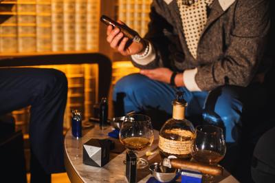 Verre de cognac, bouteille en arrière-plan, cigare allumé posé sur un cendrier et briquet sur une table en marbre.