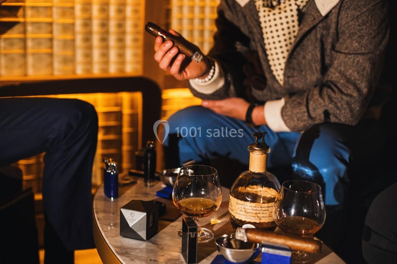 Deux personnes assises autour d'une table avec des cigares, des verres de spiritueux et des accessoires.