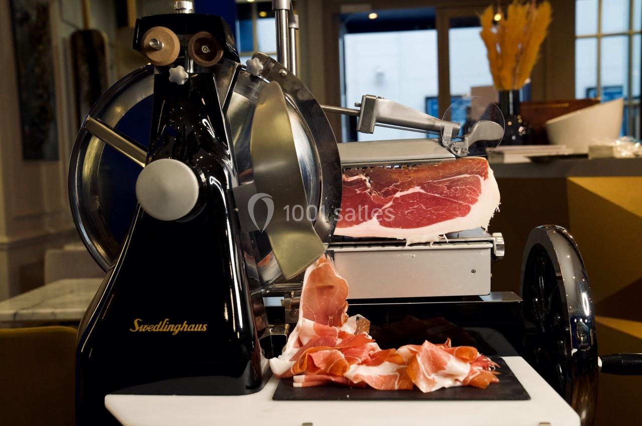 Trancheuse à jambon en métal noir avec une pièce de jambon cru et des tranches fines disposées sur une planche.