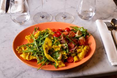 Saucisson sec artisanal suspendu dans un filet devant des bouteilles de vin en arrière-plan flou.