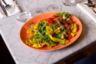 Saucisson sec artisanal suspendu dans un filet devant des bouteilles de vin en arrière-plan flou.