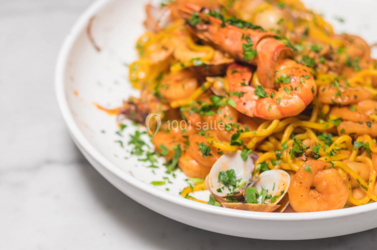 Assiette de pâtes aux fruits de mer avec crevettes, palourdes et persil, servie sur une table en marbre.