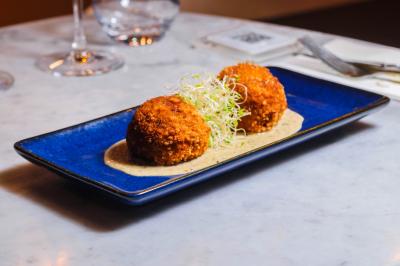Saucisson sec artisanal suspendu dans un filet devant des bouteilles de vin en arrière-plan flou.