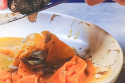 Saucisson sec artisanal suspendu dans un filet devant des bouteilles de vin en arrière-plan flou.