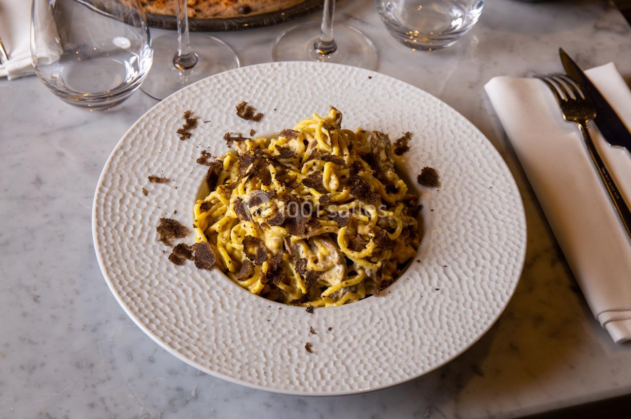 Assiette de pâtes fraîches garnies de truffes râpées, servie sur une table en marbre avec couverts et verres.