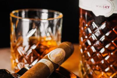 Saucisson sec artisanal suspendu dans un filet devant des bouteilles de vin en arrière-plan flou.