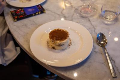 Saucisson sec artisanal suspendu dans un filet devant des bouteilles de vin en arrière-plan flou.