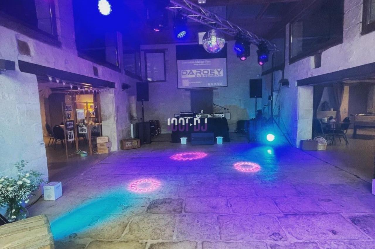 Salle en pierre avec éclairage coloré, scène équipée de projecteurs et écran en fond, ambiance festive.