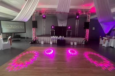 Salle de réception décorée avec une table dressée, des lumières colorées et une scène équipée pour un événement.