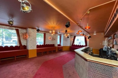 Salle avec bar, banquettes rouges, décor rétro, disques vinyles au mur et éclairage chaleureux.