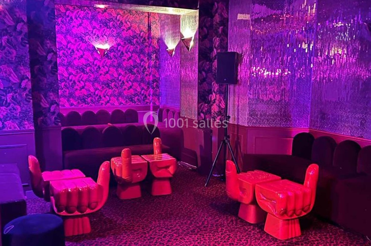 Salle au décor rétro avec des fauteuils en forme de main, tables assorties et éclairage rose tamisé.