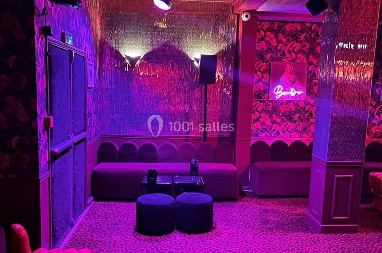 Salle aux tons roses et violets avec banquettes, poufs, murs décorés et éclairage tamisé.