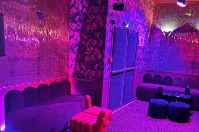 Salle avec bar, banquettes rouges, décor rétro, disques vinyles au mur et éclairage chaleureux.