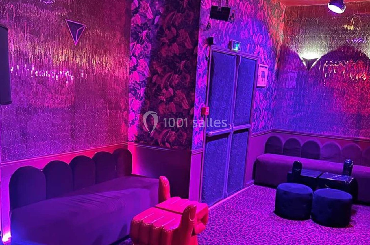 Salon coloré avec éclairage rose et violet, banquettes, poufs et murs ornés de motifs floraux et brillants.