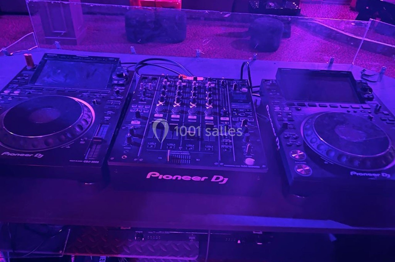 Matériel de DJ comprenant une table de mixage et deux platines Pioneer sur une table dans un environnement sombre.