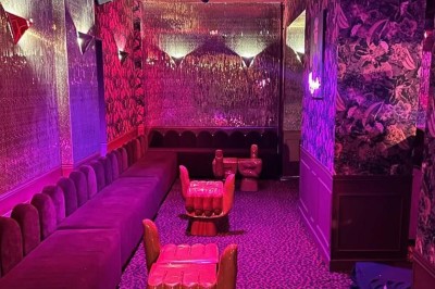 Salle avec moquette rouge, banquettes le long des murs, bar en angle et luminaires suspendus dans un décor rétro.