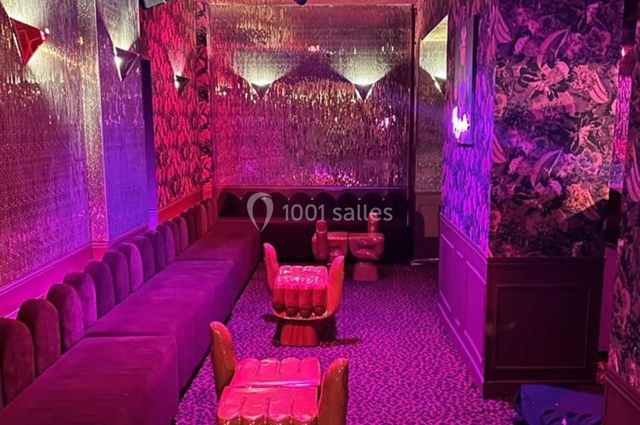 Salle lounge avec banquettes rouges, fauteuils originaux et éclairage tamisé aux tons roses et violets.