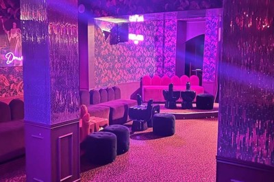 Salle avec moquette rouge, banquettes le long des murs, bar en angle et luminaires suspendus dans un décor rétro.