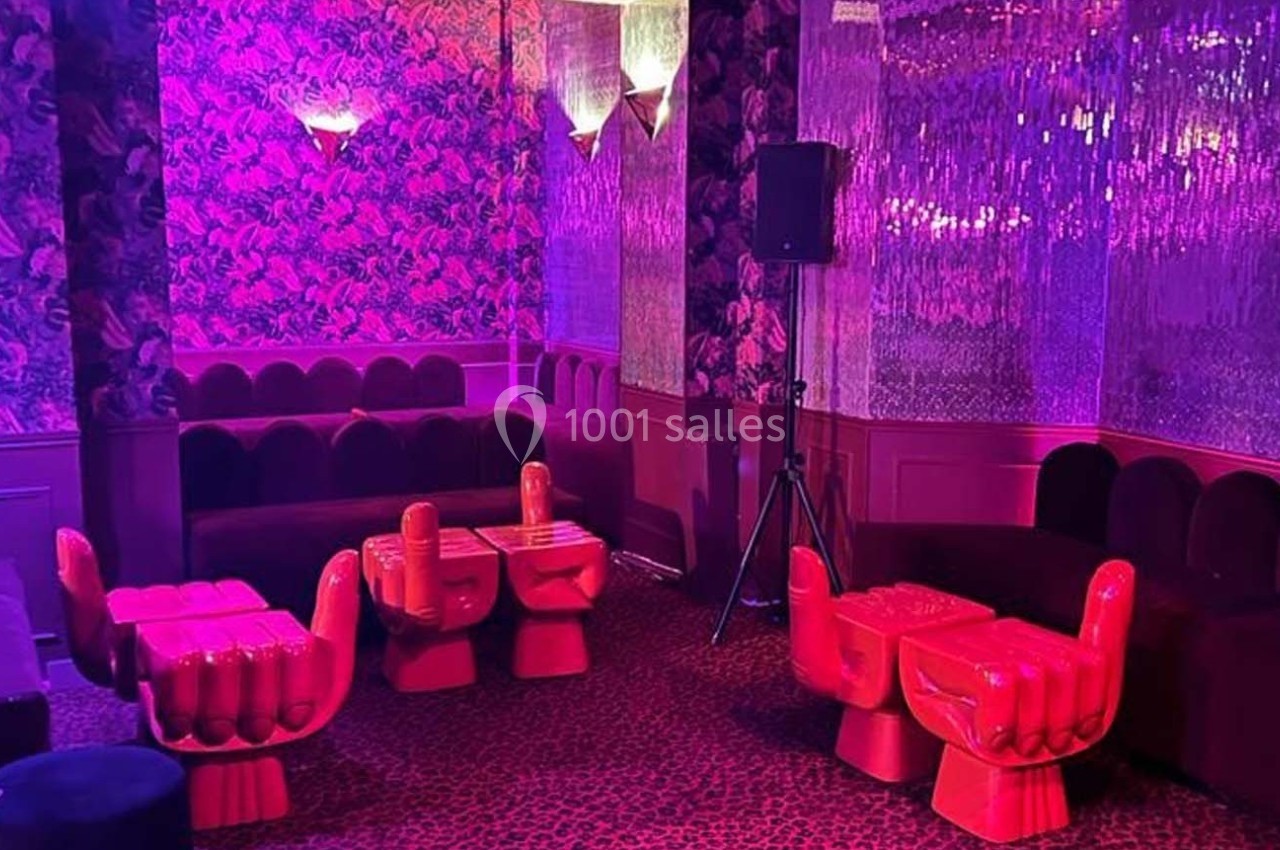 Salle colorée avec fauteuils en forme de main rouges, tables assorties, murs à motifs et éclairage rose tamisé.