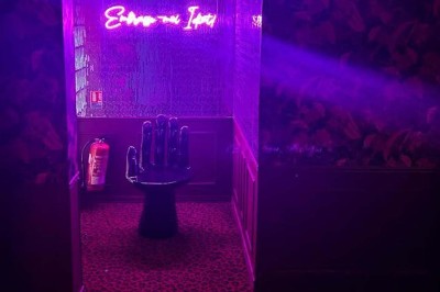 Salle avec moquette rouge, banquettes le long des murs, bar en angle et luminaires suspendus dans un décor rétro.