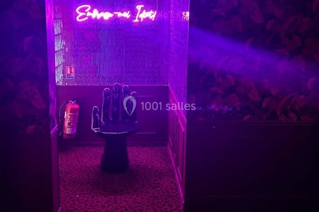 Chaise en forme de main noire dans un couloir éclairé par une lumière violette avec un néon et un extincteur au mur.