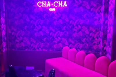 Salle avec moquette rouge, banquettes le long des murs, bar en angle et luminaires suspendus dans un décor rétro.