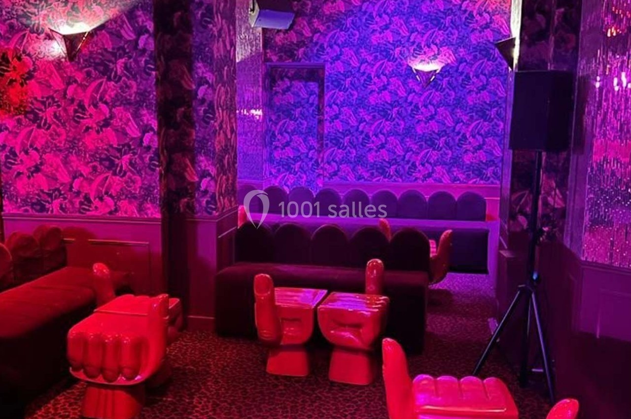 Salle aux murs tapissés de motifs colorés, éclairée par une lumière rose, avec des fauteuils en forme de mains.