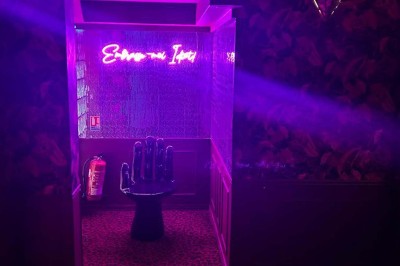 Salle avec moquette rouge, banquettes le long des murs, bar en angle et luminaires suspendus dans un décor rétro.