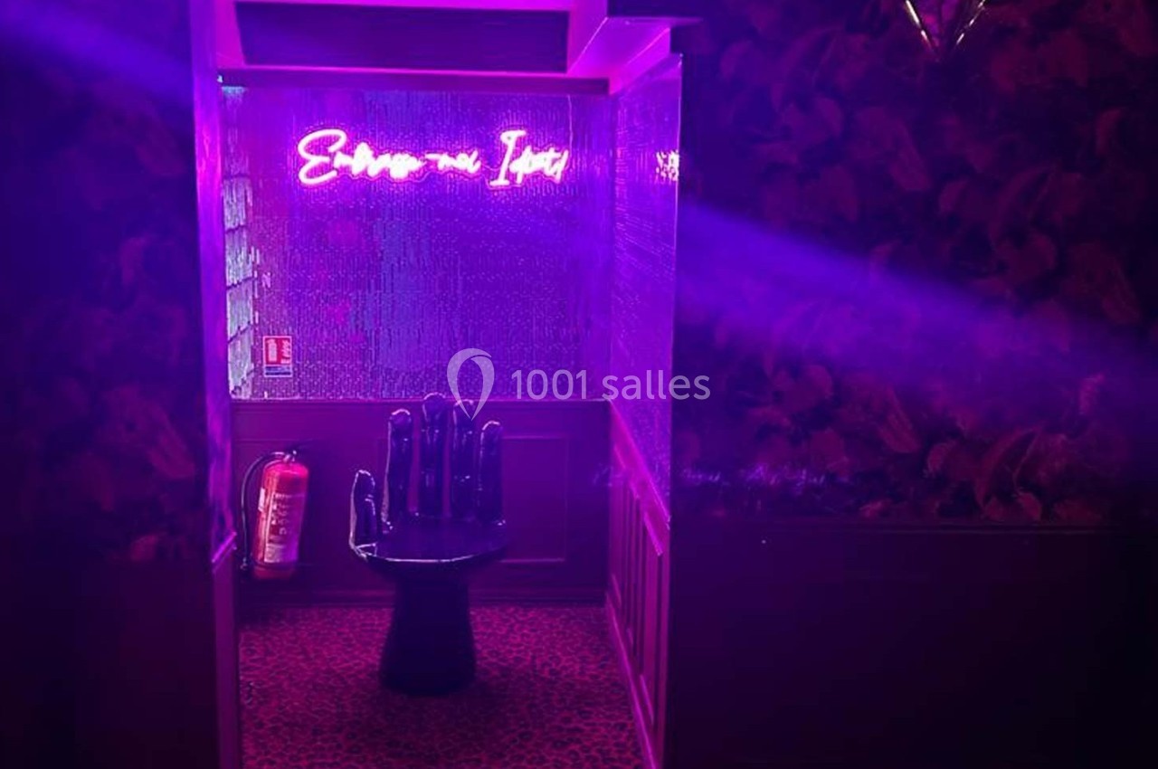 Fauteuil en forme de main noire dans une pièce éclairée par une lumière violette avec un néon rose au mur.