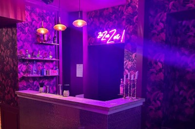 Salle avec moquette rouge, banquettes le long des murs, bar en angle et luminaires suspendus dans un décor rétro.