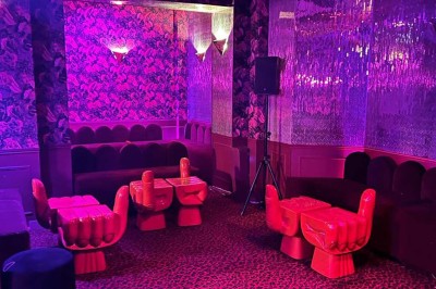 Salle avec moquette rouge, banquettes le long des murs, bar en angle et luminaires suspendus dans un décor rétro.