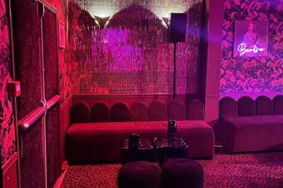 Salle avec moquette rouge, banquettes le long des murs, bar en angle et luminaires suspendus dans un décor rétro.
