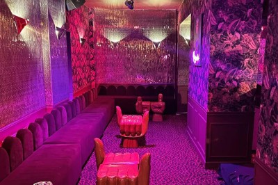 Salle avec moquette rouge, banquettes le long des murs, bar en angle et luminaires suspendus dans un décor rétro.