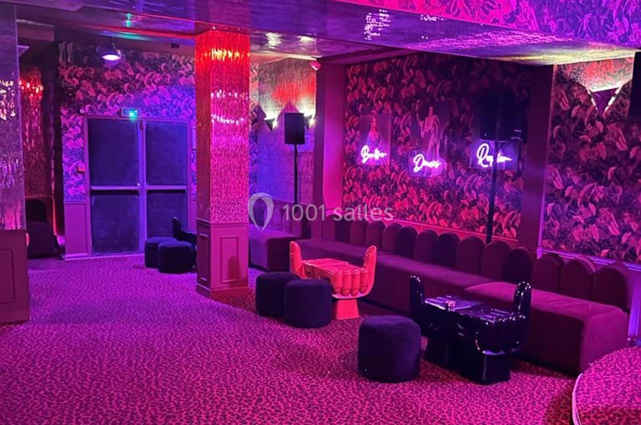 Salle lounge avec banquettes rouges, poufs noirs, murs décorés de motifs floraux et éclairage rose néon.