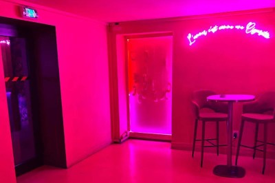 Salle avec moquette rouge, banquettes le long des murs, bar en angle et luminaires suspendus dans un décor rétro.