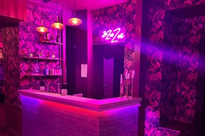 Salle avec moquette rouge, banquettes le long des murs, bar en angle et luminaires suspendus dans un décor rétro.