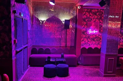 Salle avec moquette rouge, banquettes le long des murs, bar en angle et luminaires suspendus dans un décor rétro.