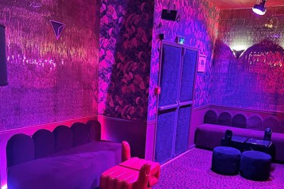 Salle avec moquette rouge, banquettes le long des murs, bar en angle et luminaires suspendus dans un décor rétro.