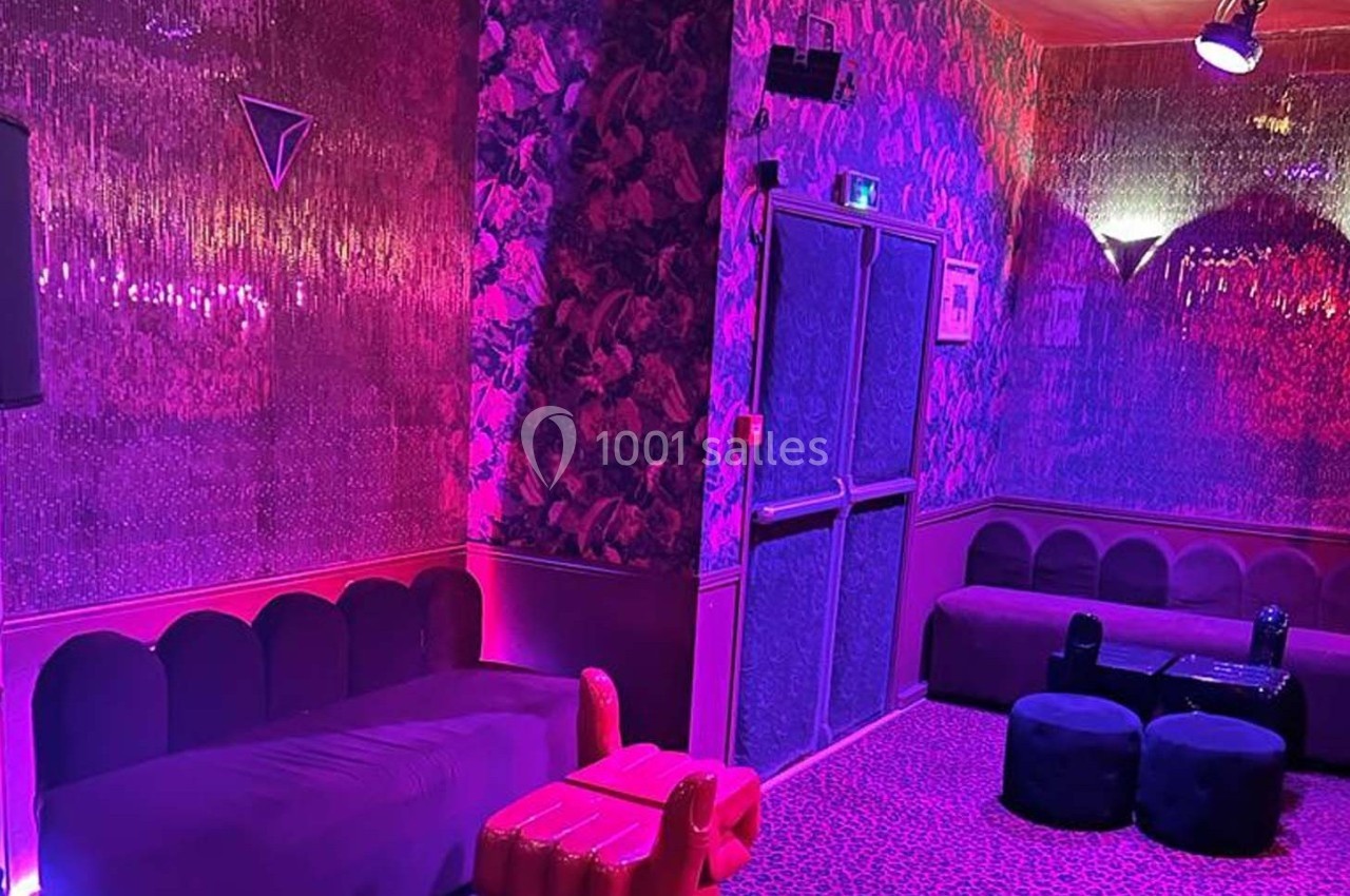 Salle décorée avec des murs texturés, éclairage rose et violet, banquettes et poufs dans un style lounge.