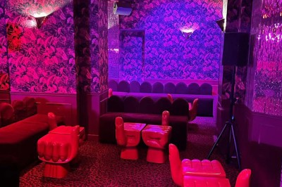 Salle avec moquette rouge, banquettes le long des murs, bar en angle et luminaires suspendus dans un décor rétro.