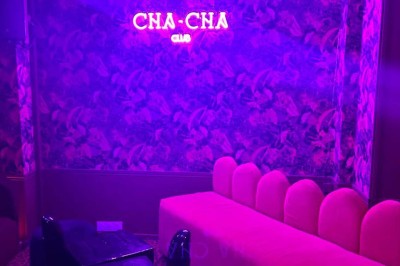 Salle avec moquette rouge, banquettes le long des murs, bar en angle et luminaires suspendus dans un décor rétro.