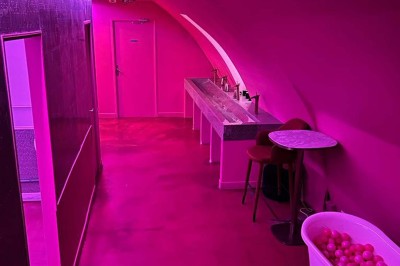 Salle avec moquette rouge, banquettes le long des murs, bar en angle et luminaires suspendus dans un décor rétro.