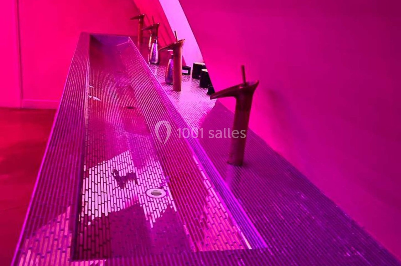 Lavabo moderne en mosaïque violette avec robinets design, éclairé par une lumière rose.