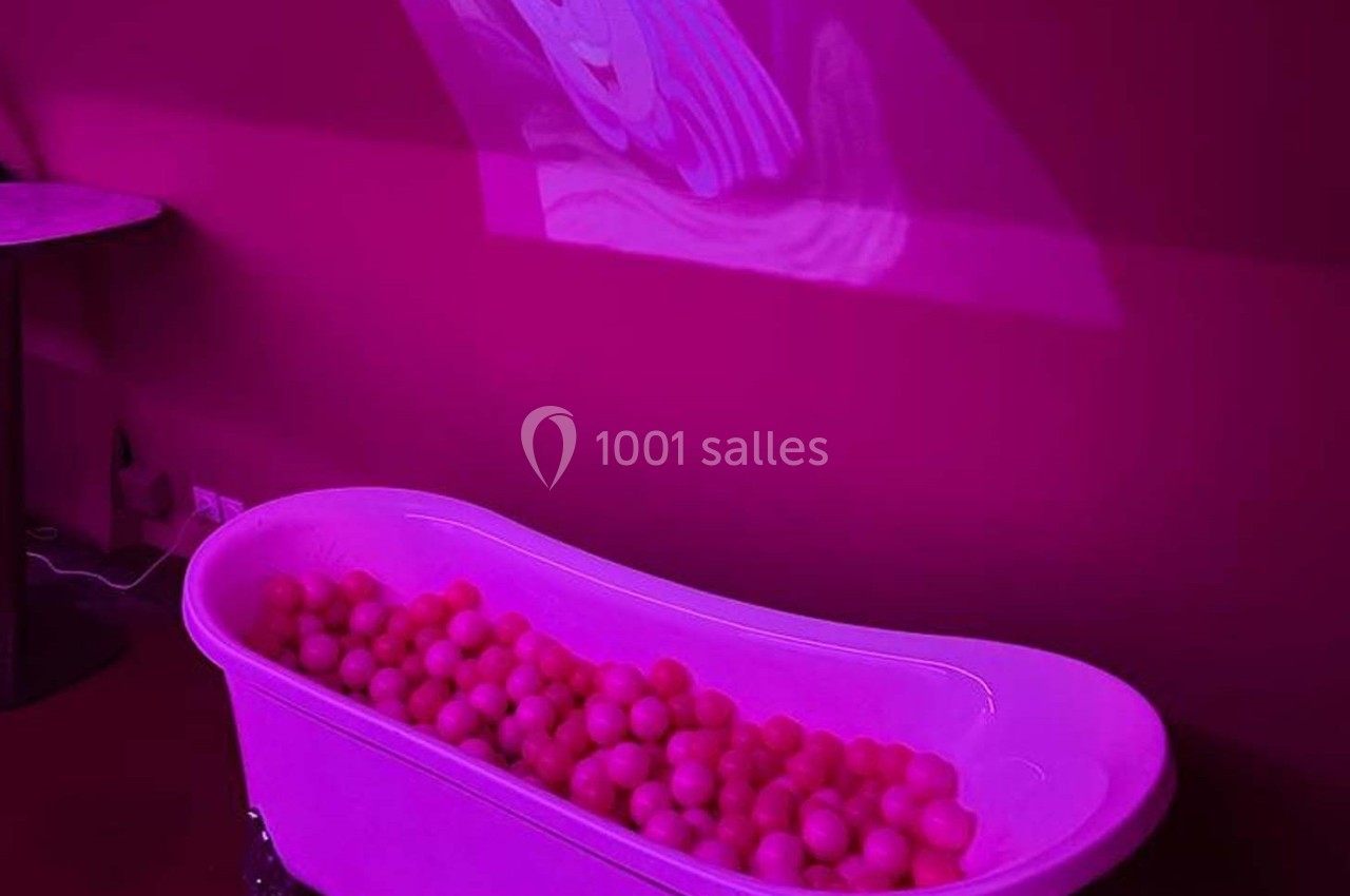 Baignoire remplie de balles roses dans une pièce éclairée par une lumière rose avec une projection murale floue.