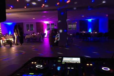 Salle de réception éclairée par des lumières colorées, avec une table de mixage au premier plan.