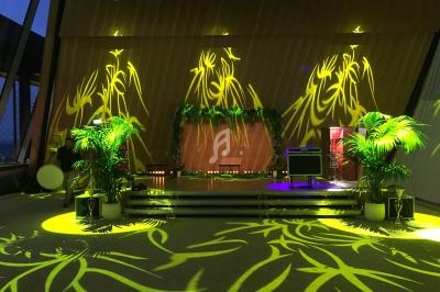 Scène décorée de plantes et illuminée par des motifs lumineux jaunes dans une salle moderne avec des murs en bois.